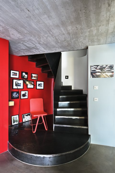 Eingangsbereich mit schwarzer Wendeltreppe und roter Wand, die mit kleinen Bilderrahmen geschmückt ist.