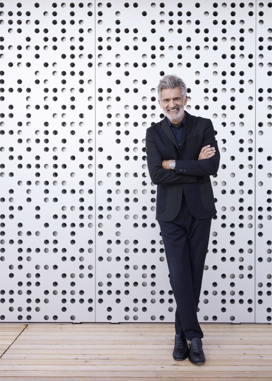 Alfredo Häberli steht in einem schwarzen Anzug vor einer gelochten Aluminiumfassade seines neuen Baufritz-Hauses.