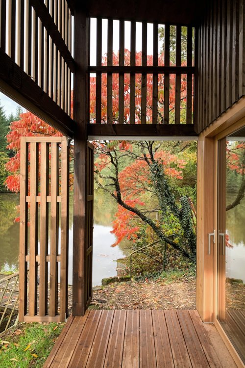 Holzterrasse mit Ausblick in die umliegende Natur, umgeben von einer gitterartigen Holzfassade mit geöffneten Türen