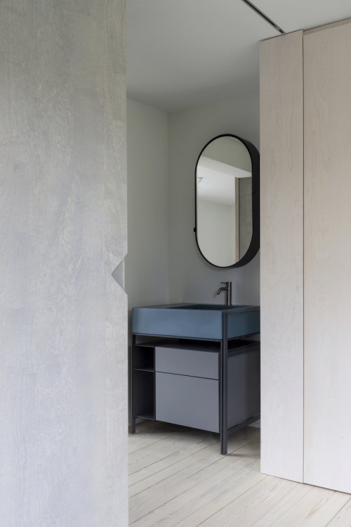 Seitlicher Blick in Bad mit ovalem Spiegel über türkis-grauem Badmöbel.