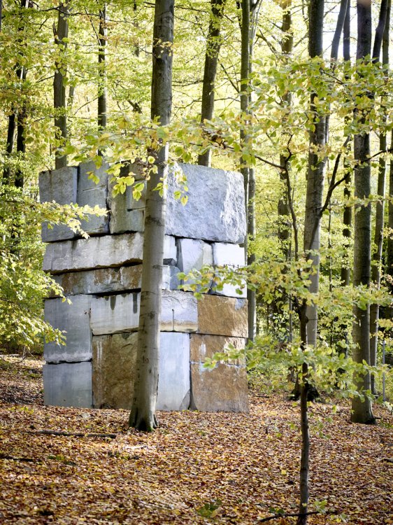 Eine Skulptur aus mehreren rechteckigen, aufeinander geschichteten Steinen im einem Laubwald