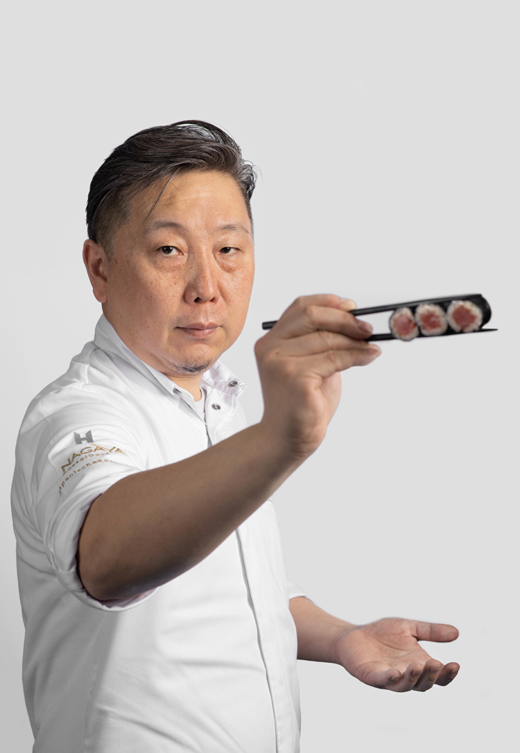 Der japanische Spitzenkoch Yoshizumi Nagaya zeigt Essstäbchen mit drei Maki in die Kamera.