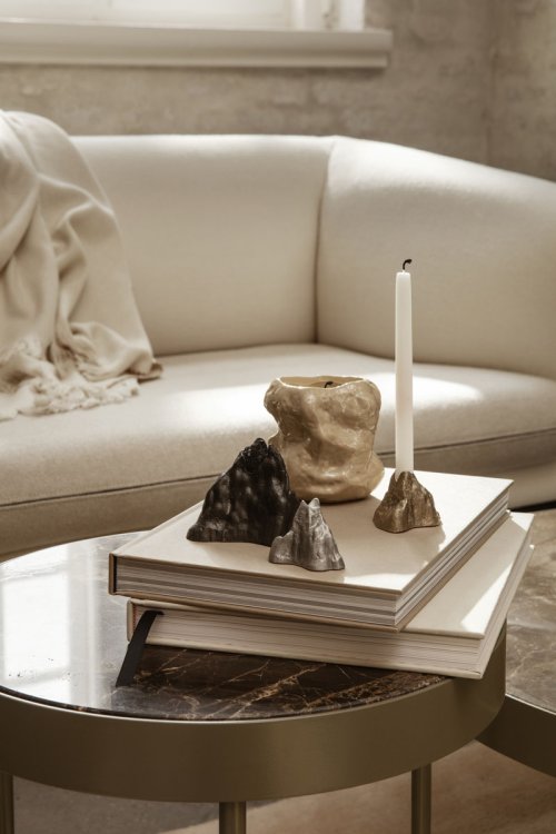 Steinartiger Kerzenhalter aus Stein in gold und silber von ferm Living auf einem Beistelltisch mit Büchern.