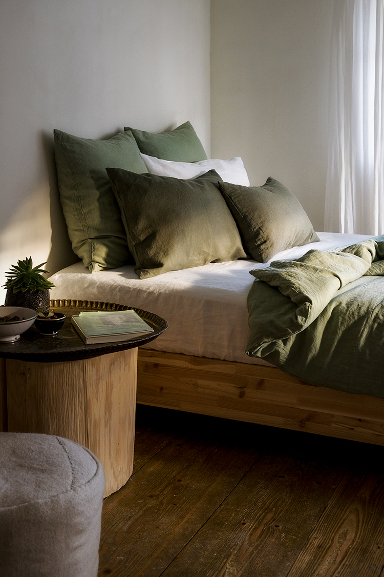 Helles Schlafzimmer mit Bett mit olivegrüner Leinenbettwäsche.