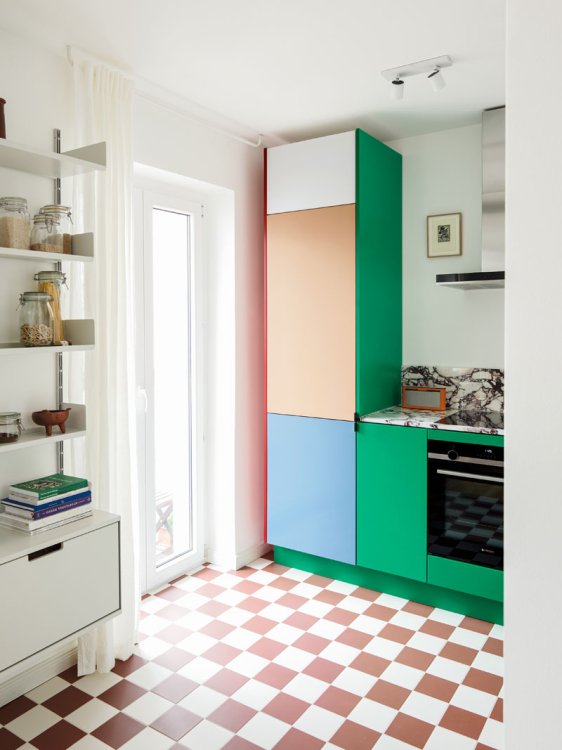 Blick in die Küche mit Terracotta weissem Kachelboden und bunter Küche mit Fronten in Lachs, Hellblau und Grün.