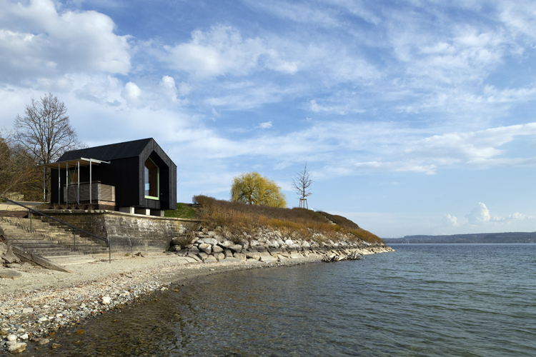 Am Bodenseeufer steht auf der linken Seite ein Tiny House, das wie ein schwarzer Monolith aussieht.