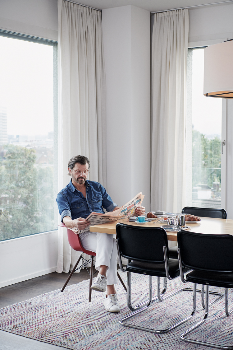 Erhard Schwendimann sitzt am Kopfende des Esstisches und liest die Zeitung. Vor ihm ist das Frühstück aufgedeckt hinter ihm sind Fenster, wo man auf Zürich sieht.