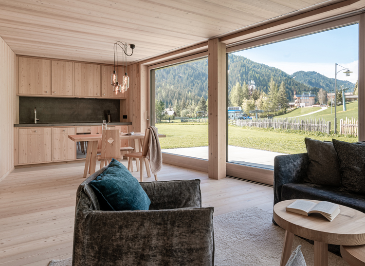 Innenansicht einer Ferienwohnung verkleidet in Lärchenholz mit Blick über Panoramafenster in die grüne Umgebung.