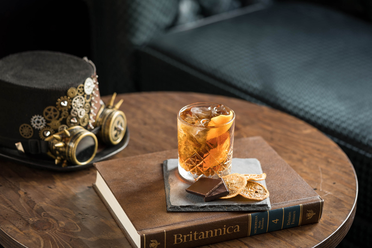 Glas Old Fashioned Dring auf Holztisch mit Hut und Brille aus Steampunk.