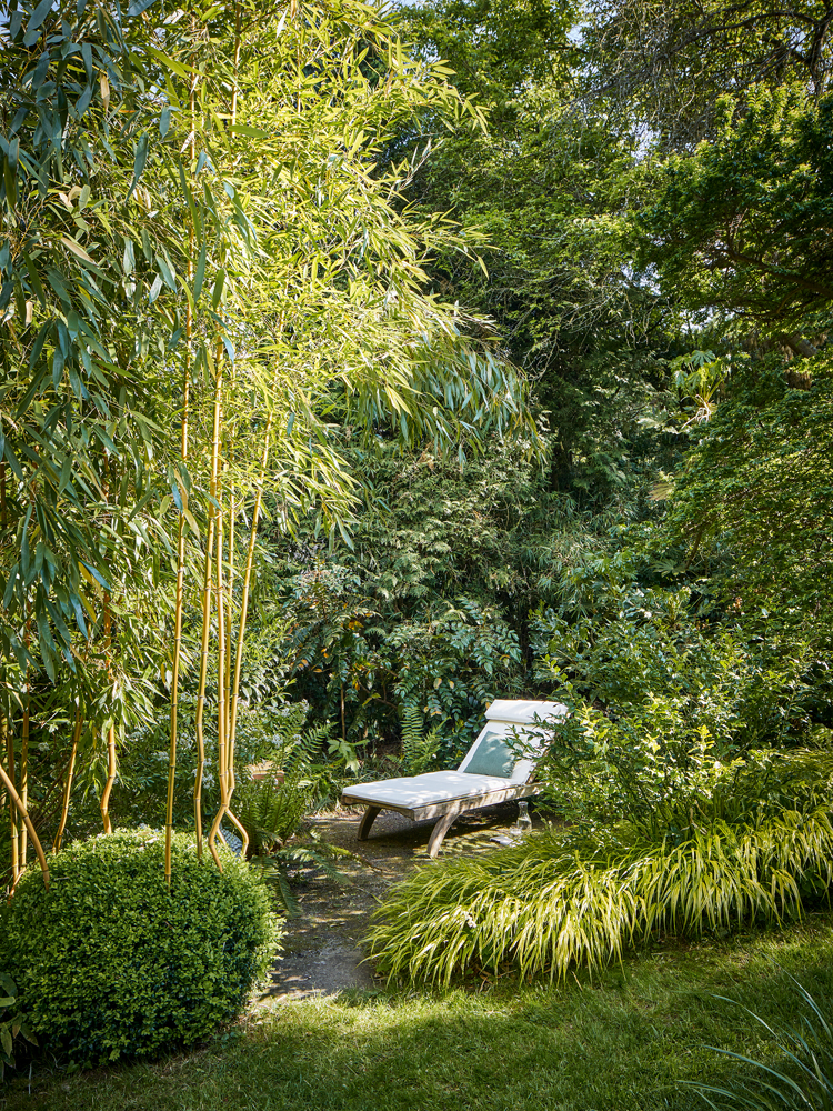 Ausblick in einen grünen, üppigen Naturgarten mit Liegestuhl aus Holz.