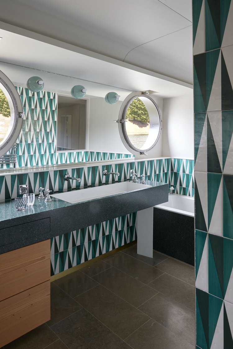 Badezimmer mit Kacheln aus grün-türkis Mosaikmuster und runden Spiegeln.