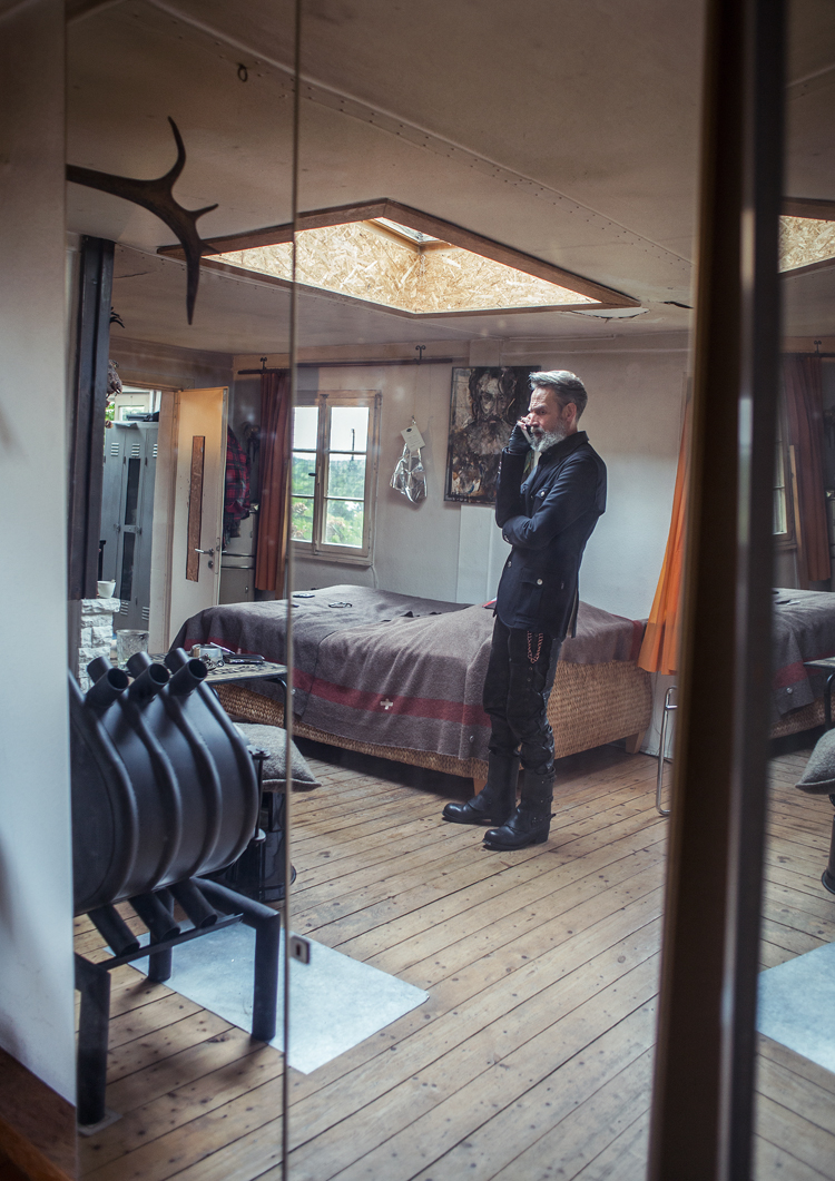 Mann steht in mitten eines Schlafzimmer vor dem Bett, in der Decke hat es ein quadratisches Dachfenster.