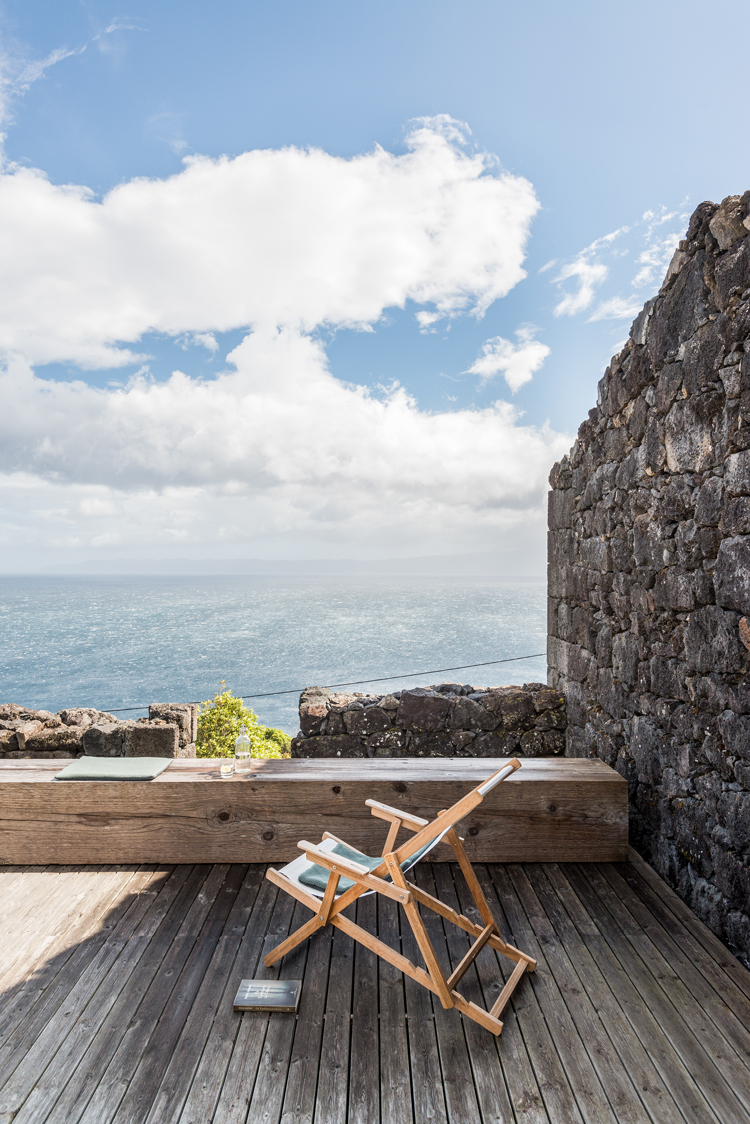 Liegestuhl steht auf minimalistischer Terasse mit altem Holzboden mit Blick aufs Meer.