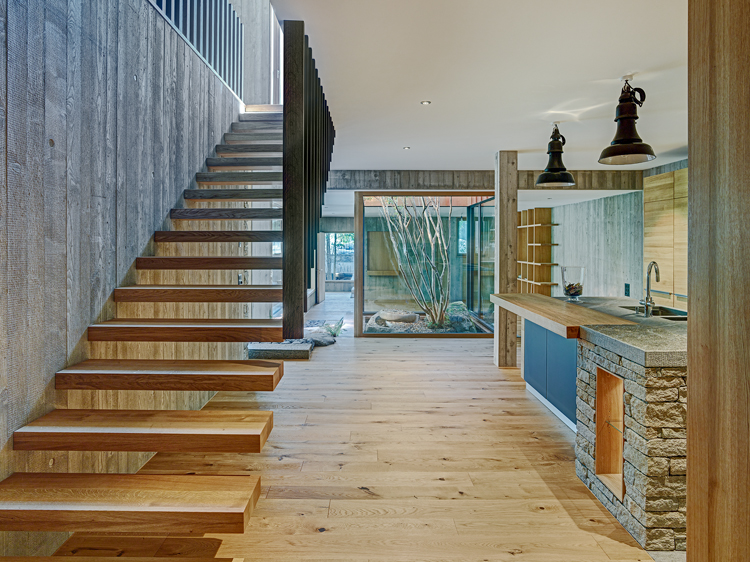 Teilansicht von Küche mit freihängender Treppe aus Holz, die ins Obergeschoss führt.