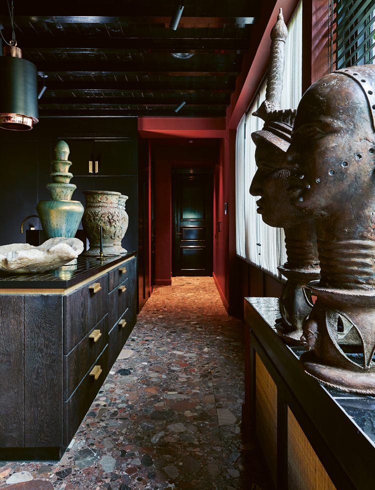 Schwarze Küchenzeile inform einer Bar mit Terazzo-Boden und antiken Figuren.