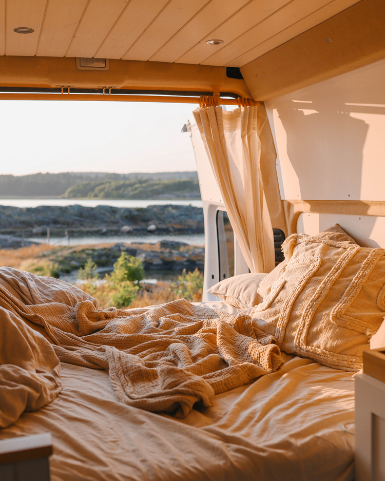 Camper-Van mit gelber Leinen-Bettwäsche und offener Campertür mit Blick in die Natur.