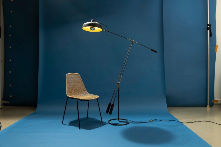 Der Basket-Chair (Entwurf: 1951) und die Movalux-Leuchte (Entwurf: 1947) von Gian Franco Legler vor blauer Wand.