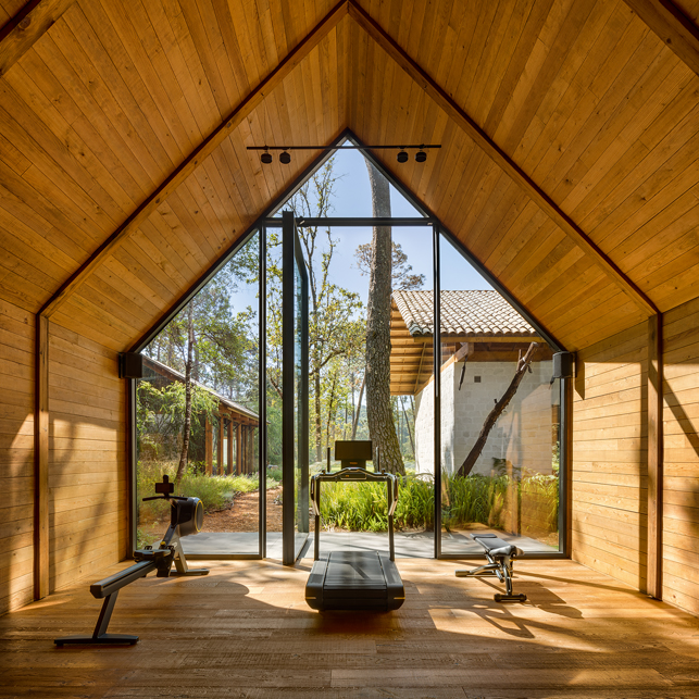 Hohe Raum mit Giebeldach und Holzdecken und Sicht ins Grüne durch deckenhohe Fenster.