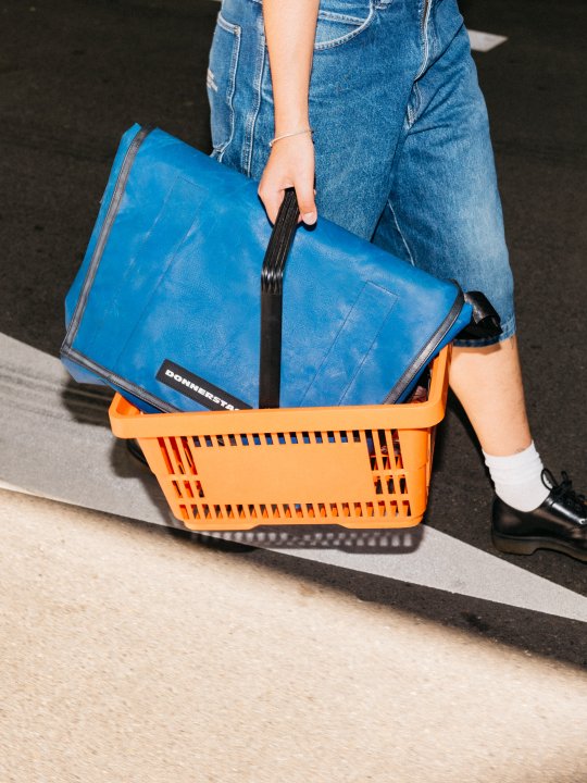 Person mit orangem Einkaufskorb, darin eine Freitag-Tasche
