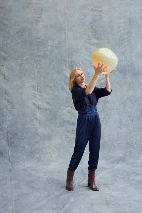 Portrait von Simone Lüling, wo sie die Leuchte Haumea Convex in die Höhe stemmt.