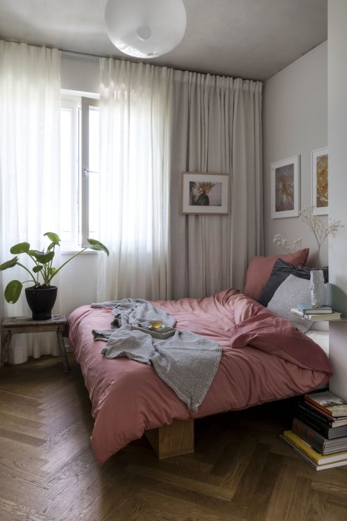 Bett mit rosa Bettbezug und verschiedenfarbigen Kissen, weisser Vorhang