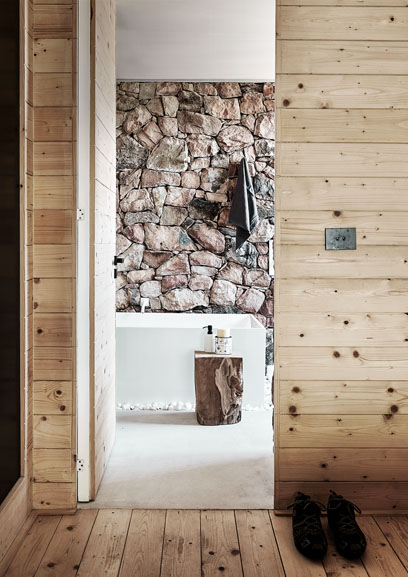 Die Tür zum Badezimmer ist geöffnet und man erkennt eine Badewanne die vor einer Wand aus Steinen besteht.