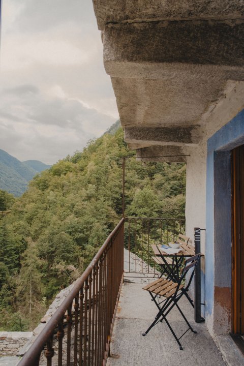 Sicht auf das bewaldete Tal von einem schmalen Balkon mit Schmiedeisengeländer und einem kleinen Balkontisch mit Stuhl.