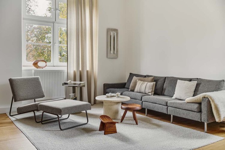 Ein Foto eines Wohnzimmer welches mit grauem Sofa, einem Tischchen und einem grauen Sessel ausgestattet ist.