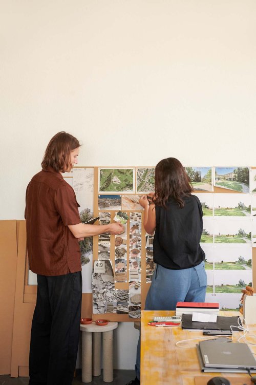Ein Mann und eine Frau die vor einer Tafel stehen und verschiedne Fotos in ihrem Atelier betrachten.