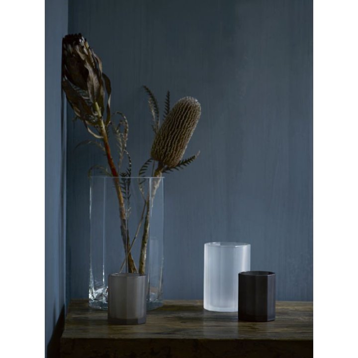 Assemblage von Vasen und Teelichtgläsern in unterschiedlicher Grösse mit getrockneten Blumen vor einer dunkelblauen Wand.