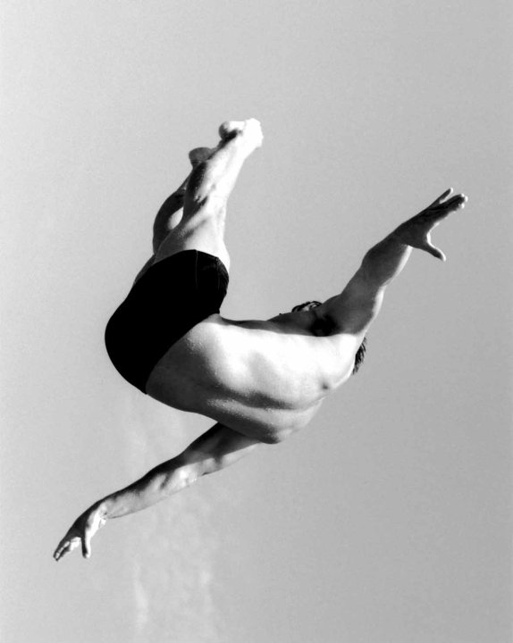 Schwarz-Weiss-Fotografie eines Salto-ausübenden Mannes in Badehose.