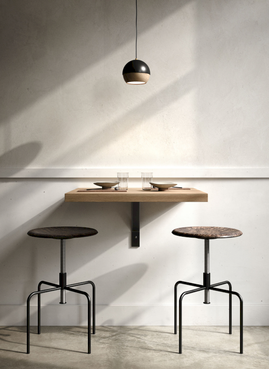 Zwei Barhocker im Industrial-Look mit runder, höhenverstellbarer Sitzfläche von Mater stehen in einem Kaffee an einem Wandtisch, über dem eine schlichte Hängelampe hängt.