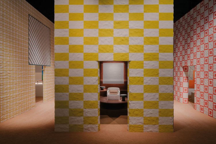 Die Installation von Hermès Home im La Pelota an der diesjährigen Ausgabe des Fuorisalone zeigt ein gelbes Lehmhaus mit gelb-weiss-kariert bemalter Fassade, neben zwei weiteren Lehmhäusern, in denen sich die neuen Kollektionen von Hermès Home befanden.