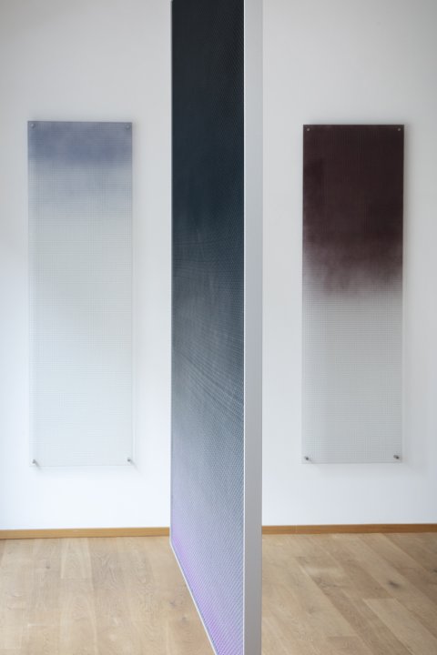 Ausstellungsraum einer Galerie mit drei abstrakten Werken von Esther Mathis im Hochformat, die verschwommene Farbverläufe in Blau-, Grau- und Rottönen zeigen.