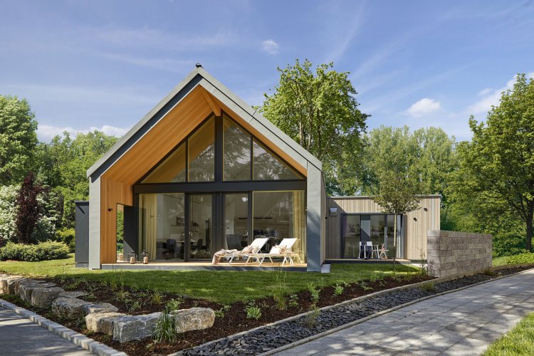 Aussenansicht des neuen Musterhaus Freiraum von Baufritz mit vorgezogenem Dach und grossflächiger Glasfassade steht in einem kompakten grünen Garten.