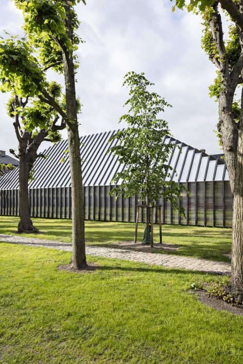 Ein Pavillon mit Satteldach aus schwarz gebeizten Holzträgern und transluzentem Polykarbonat steht auf einer grünen Wiese im Hof des Designmuseums Dänemarks.