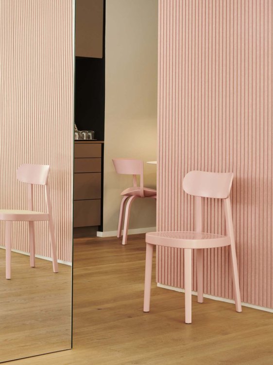 Zwei rosa Thonet-Stühle stehen in einem Raum mit Holzparkett und rosa gestrichener Wand, sowie einer Spiegelwand.