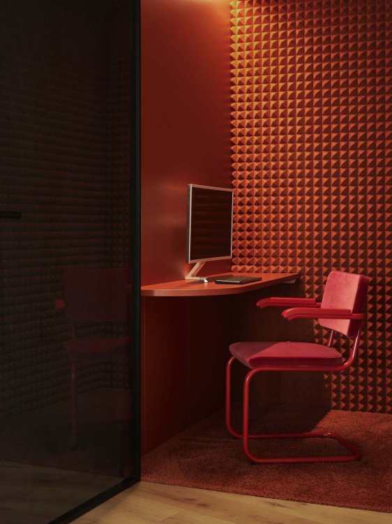 Eine spärlich beleuchtete Arbeitsecke mit roten Wänden, rotem Ecktisch und einem Computer, an dem ein ebenfalls roter Freischwingerstuhl von Thonet steht.