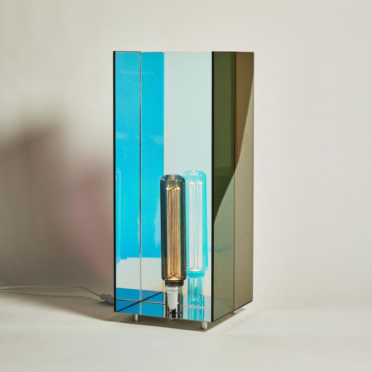 Eine quadratische Tischlampe aus türkisblau refletierenden Spiegelscheiben.