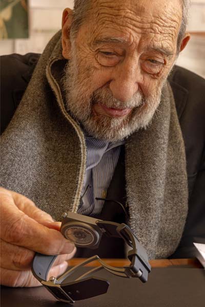 Der Architekt Alvaro Siza hält eine von ihm entworfene Uhr mit rechteckigem Ziffernblatt in der Hand.