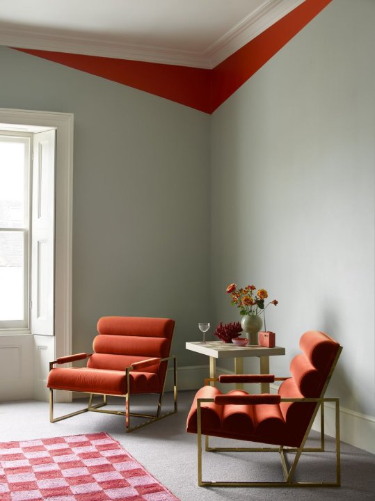 Ein Wohnzimmer mit roten Sesseln, rot kariertem Teppich und einem rot gestrichenen Wandstreifen in einem ansonsten in kühlen Grünten gehaltenem Wohnzimmer.