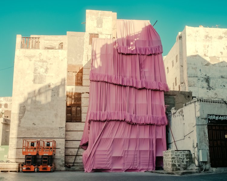 Zu sehen ist die Installation «Take Over Jeddah» von Andrés Reisinger. Es sind rosa Stoffbahnen, die entlang eines Baugerüsts ein baufälliges Haus einfassen.