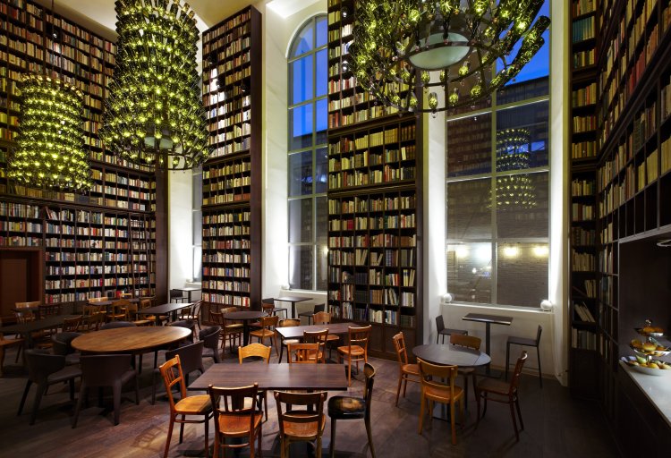 Hohe Bücherregale prallvoll mit Büchern und grosse Kronleuchter aus Bierflaschen, die von der Decke der «Library» des B2 Hotels ragen